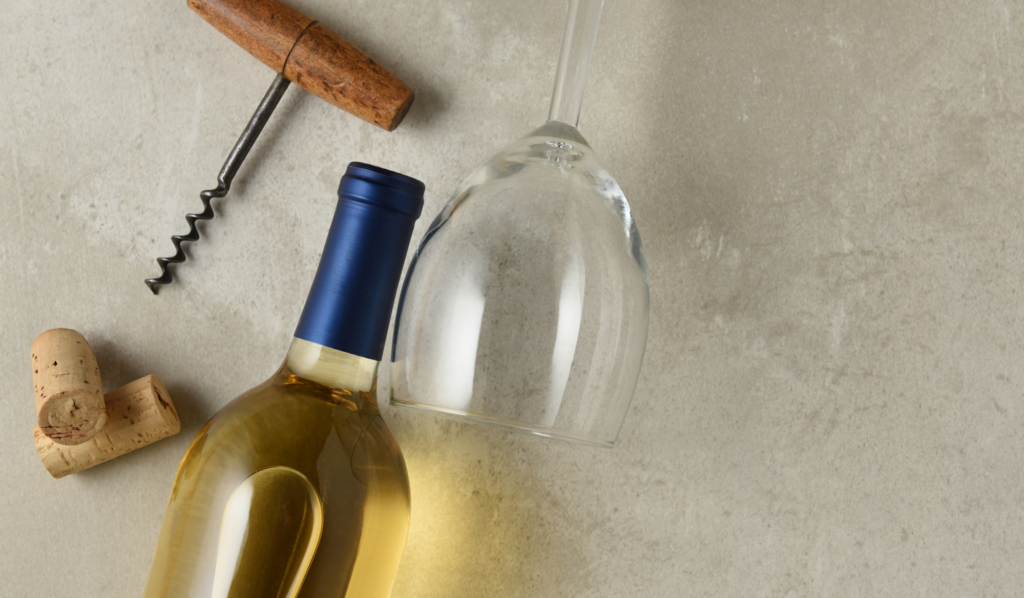 White wine bottle with corkscrew, corks, and upside-down wine glass on table