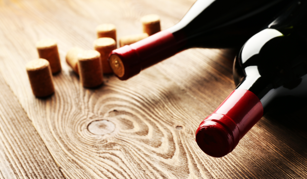Red wine bottles and natural corks scattered on rustic wood surface