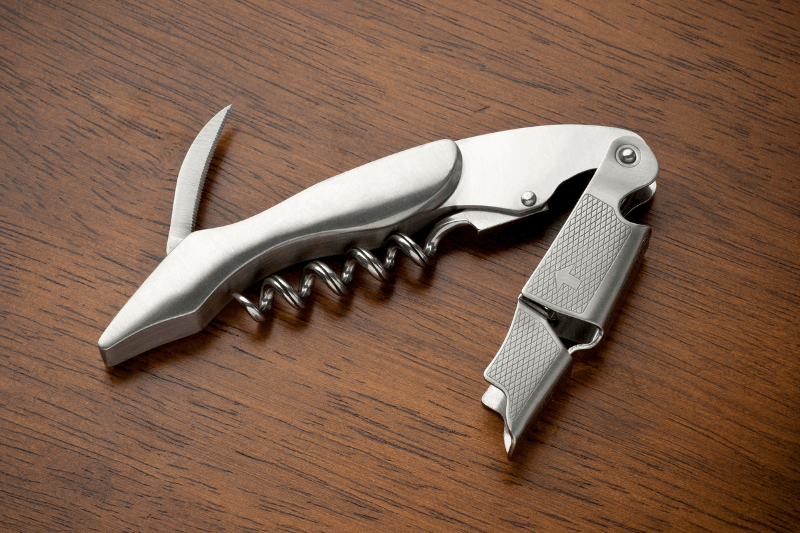 Waiter’s corkscrew with built-in foil cutter on table, showing wine key tool components