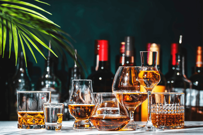 Assorted whiskey glasses and liquor bottles displayed on a table with a bar backdrop