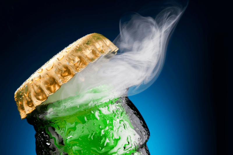 Close-up of a chilled beer bottle being opened with condensation and vapor escaping from the cap