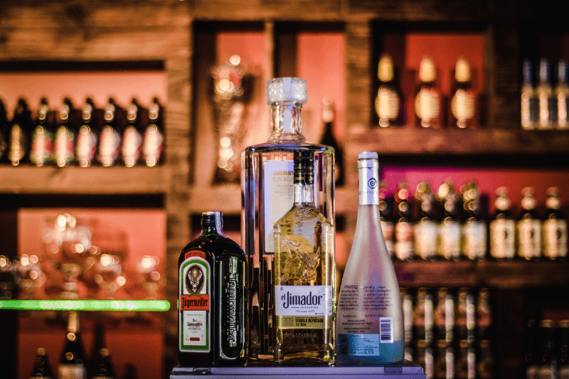 Selection of premium liquor bottles on a bar counter with a softly lit back bar showcasing various spirits in the background
