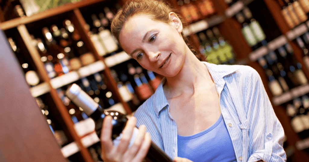 Woman holding and reading the label of a wine bottle inside a wine shop