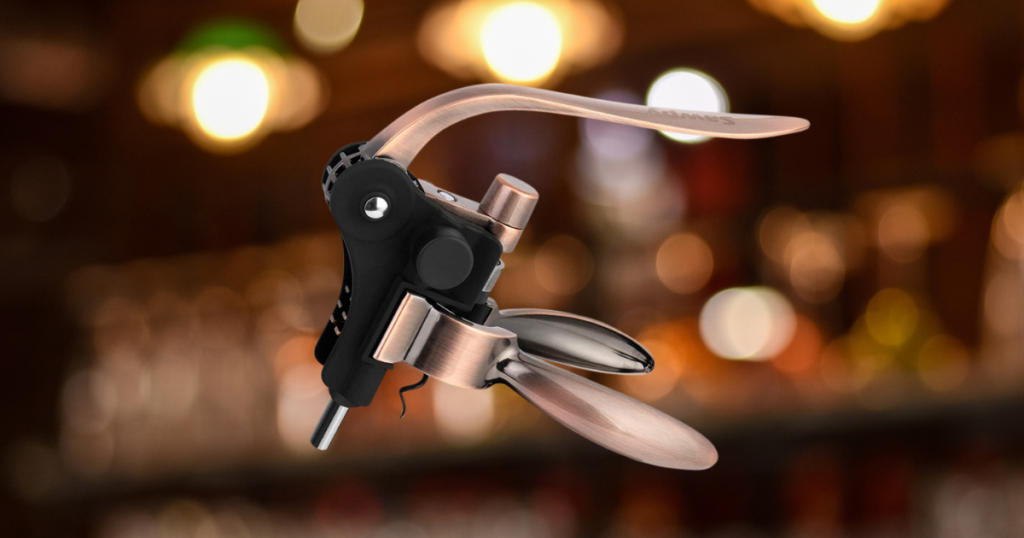 Modern stainless steel and black wine key or waiter's corkscrew with curved blade and spiral, photographed against a blurred warm-toned background