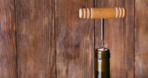 Vintage wooden-handled corkscrew with metal spiral and decorative bands on the handle, displayed against a rustic wooden background