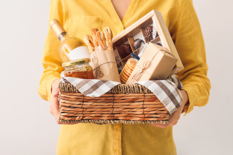 Person holding wine gift basket with snacks, jar, and boxed treats.
