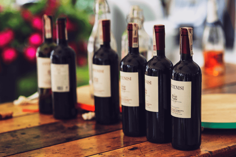 Row of red wine bottles lined up on wooden table.