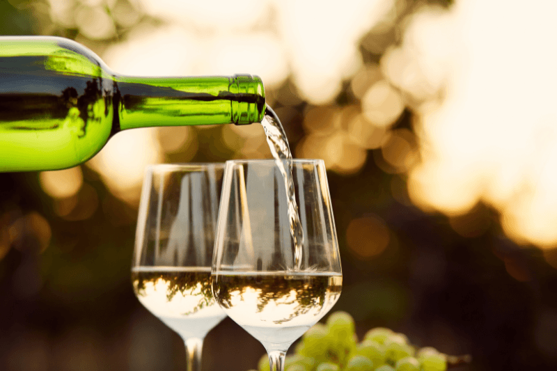 Dry white wine being poured into glasses with grapes in the background