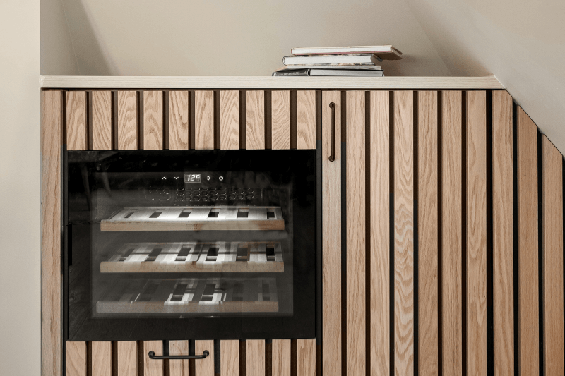 Built-in wine cooler inside a wooden cabinet under the stairs
