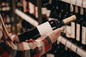 Person holding an unopened red wine bottle while shopping in a wine store