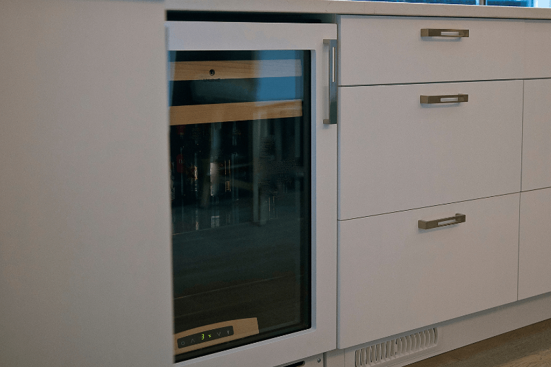 Under-counter wine cooler with glass door installed beside white kitchen drawers